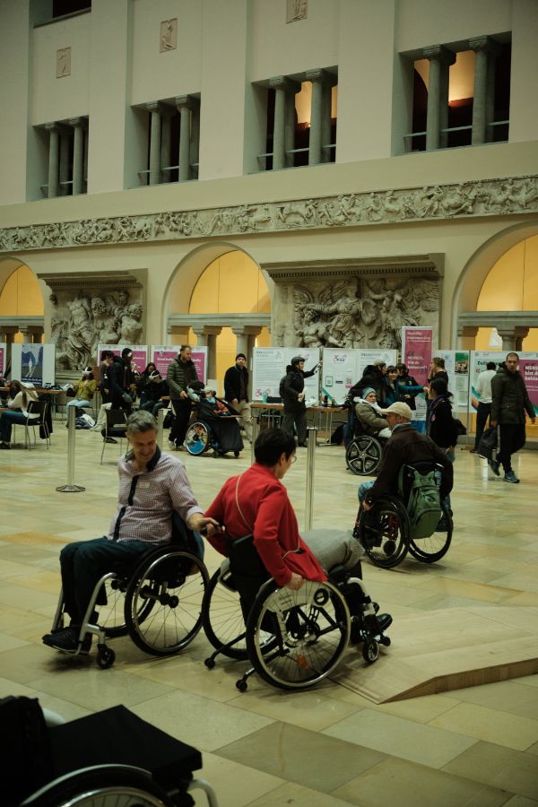 Rollstuhlparcours: Ansicht des Lichthofs der UZH mit vielen Menschen, im Vordergrund die Prorektorin Lehre und Studium, Gabriele Siegert, auf dem Rollstuhlparcour.